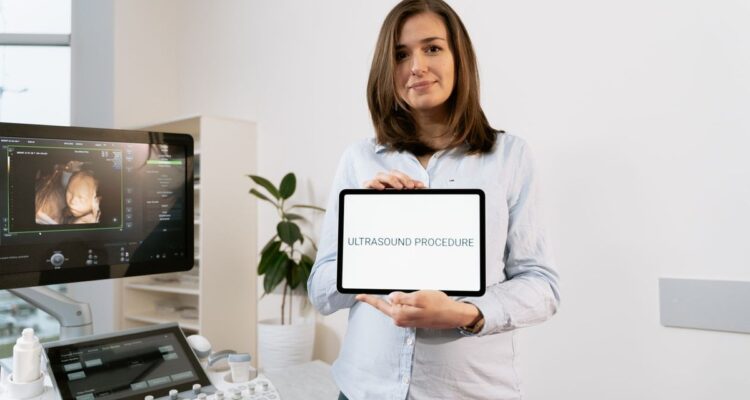 Woman holding a tablet labeled ultrasound procedure beside a clinic ultrasound machine showing a scan